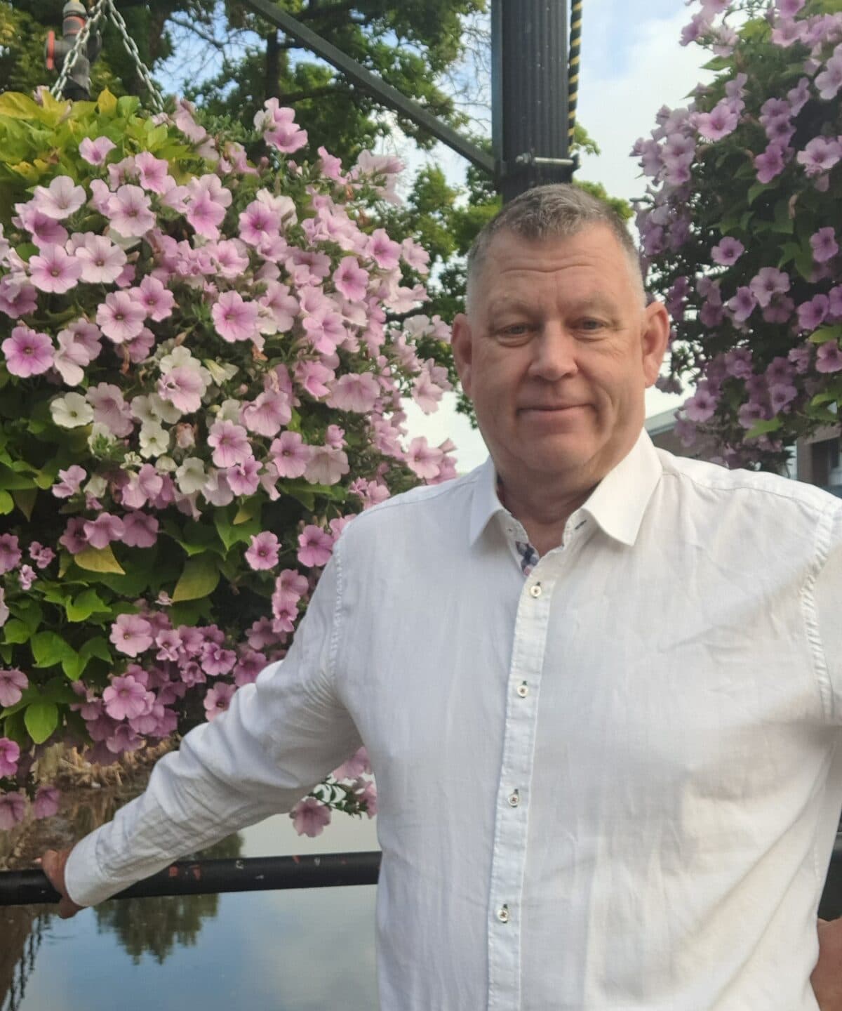 Peter i vit skjorta framför en hängande amplel med rosa och vita petunior